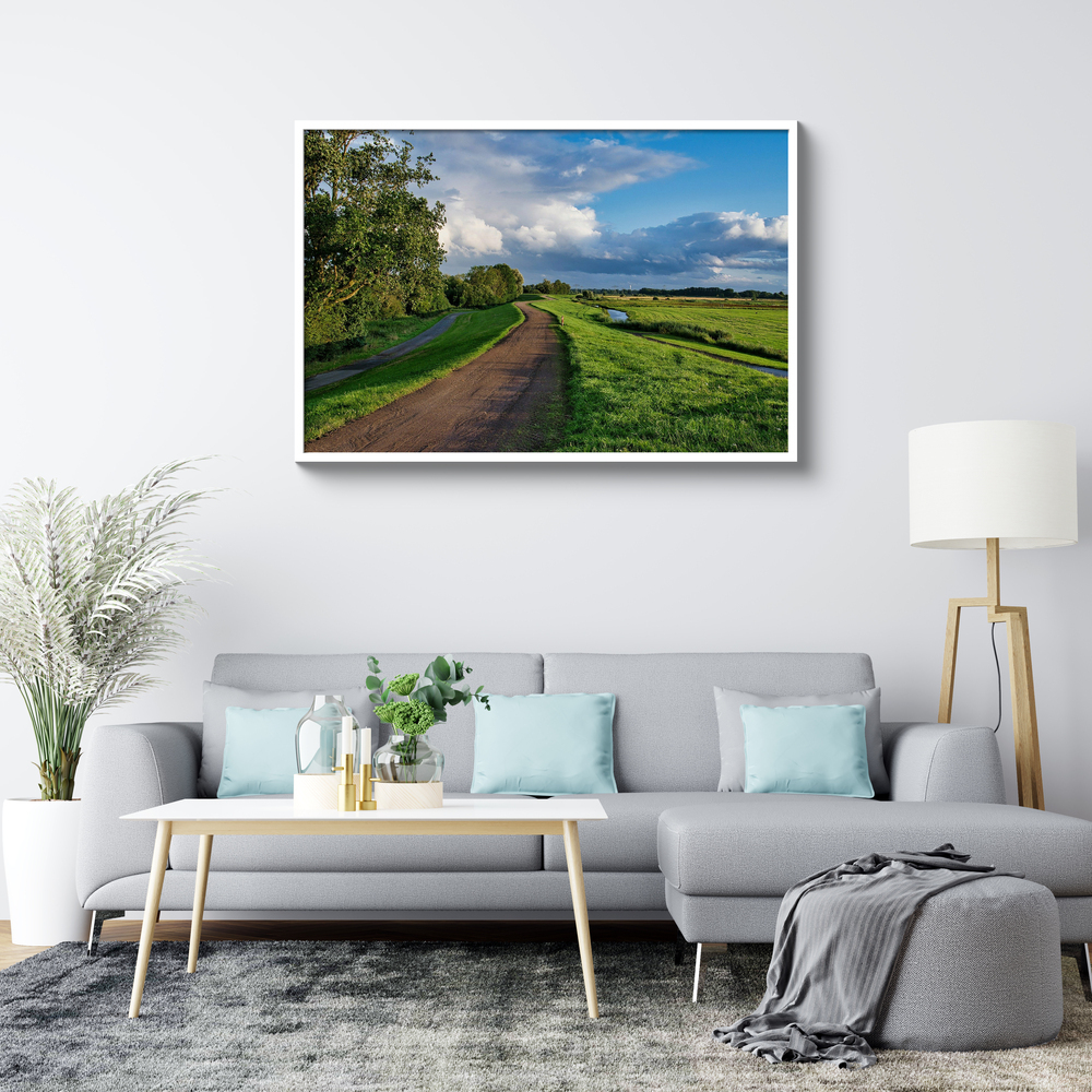 Landschaftsfoto hinter Acrylglas mit weißem Rahmen über einem grauen Sofa im hellen Wohnzimmer