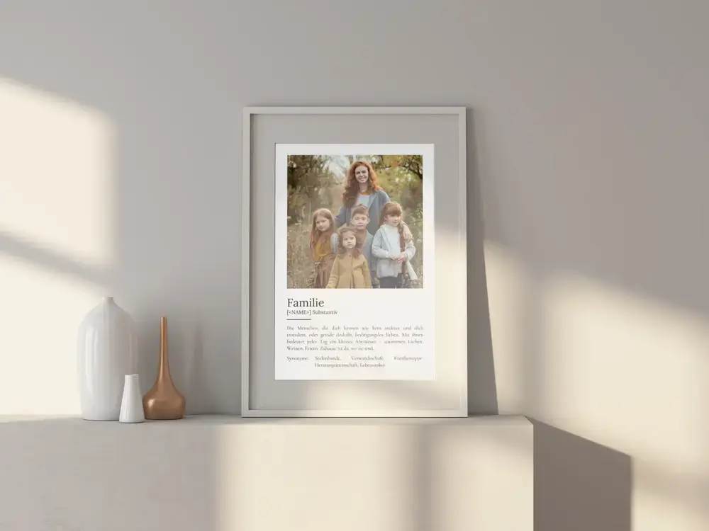 Weiß gerahmtes Definitionsposter mit Familienporträt auf einem hellen Sideboard neben dekorativen Vasen