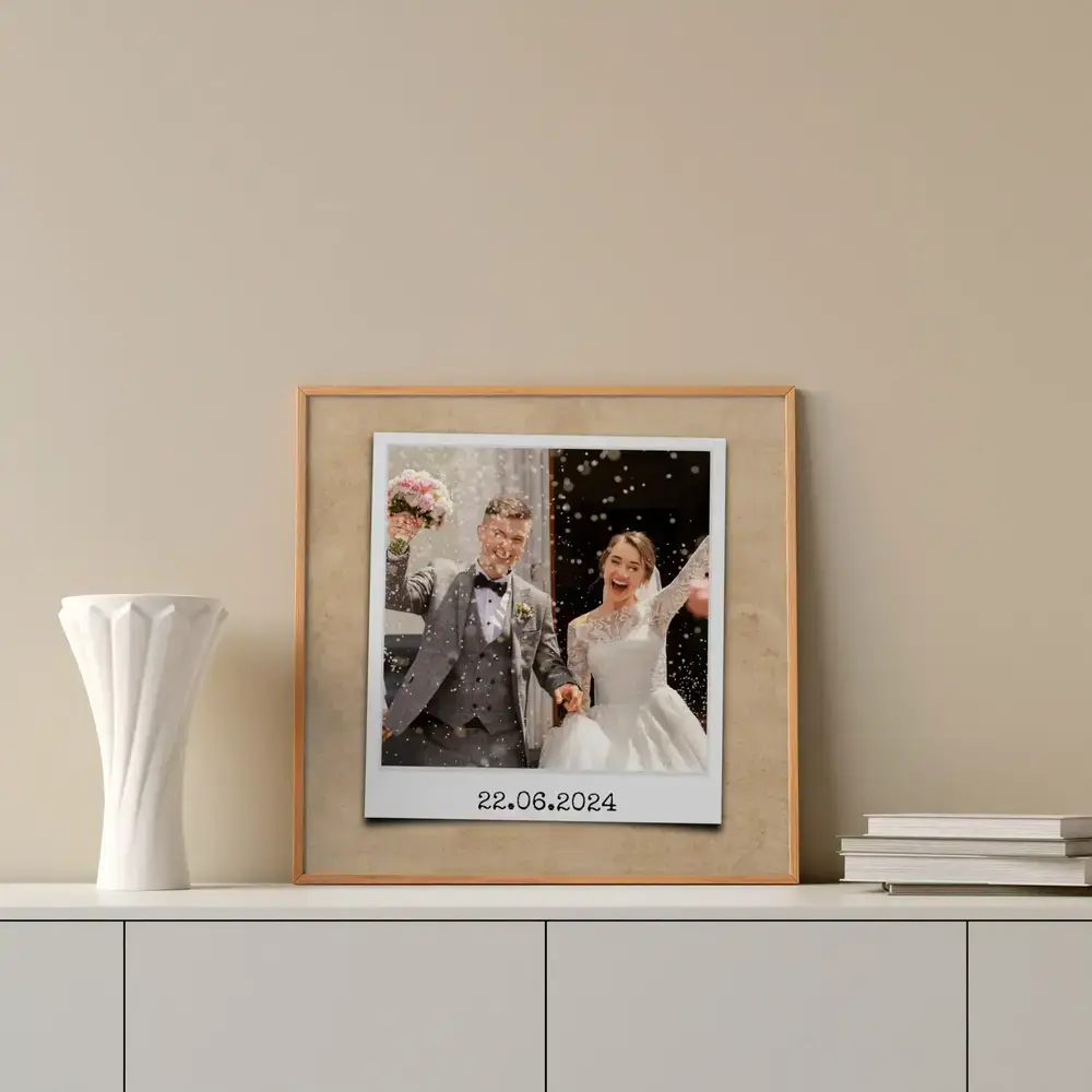 Gerahmtes Hochzeitsfoto im Sofortbild-Stil mit Datum auf weißem Sideboard neben einer Vase