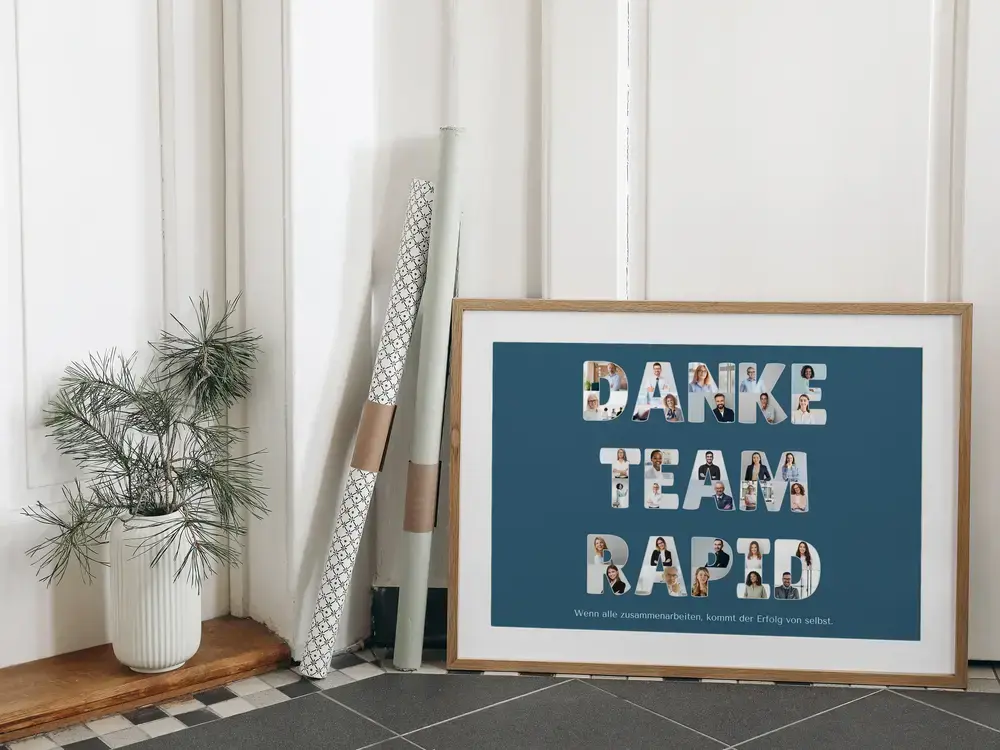 Fotocollage fürs Team mit Porträts in Buchstaben auf Petrol, im Holzrahmen am Boden neben Pflanze und Papierrollen
