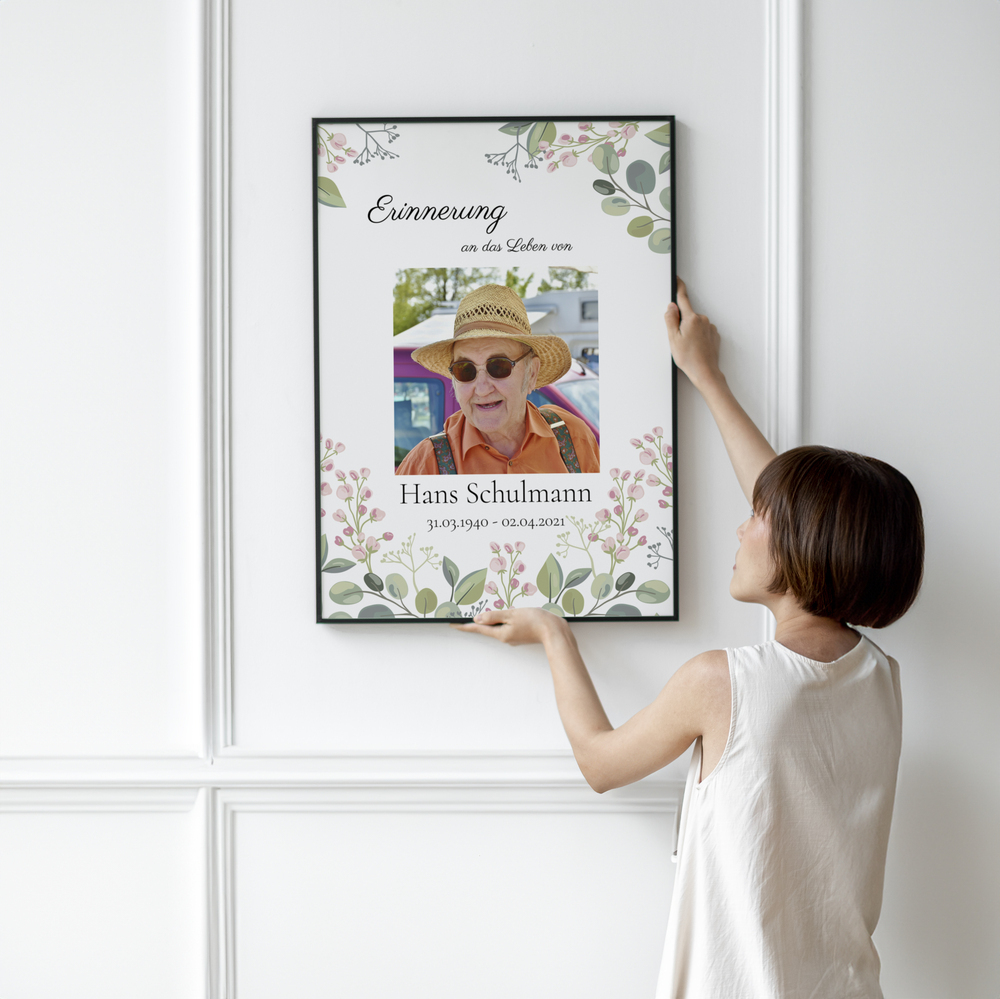Trauerfoto mit Porträt und Blumenmotiv im schwarzen Rahmen an einer weißen Wand mit Zierleisten